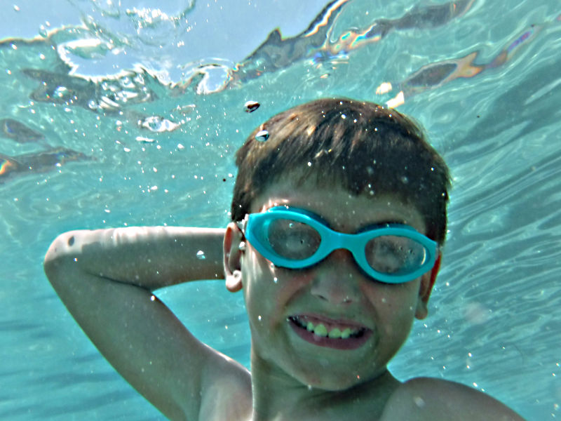 Photo: young boy wearing swim goggles, underwater in pool