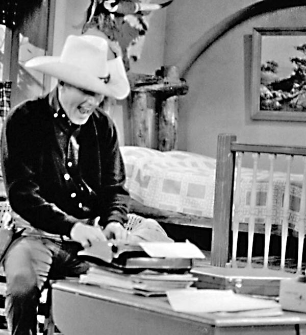 Dick van Dyke dressed as a cowboy, sitting in front of a typewriter, and grinning