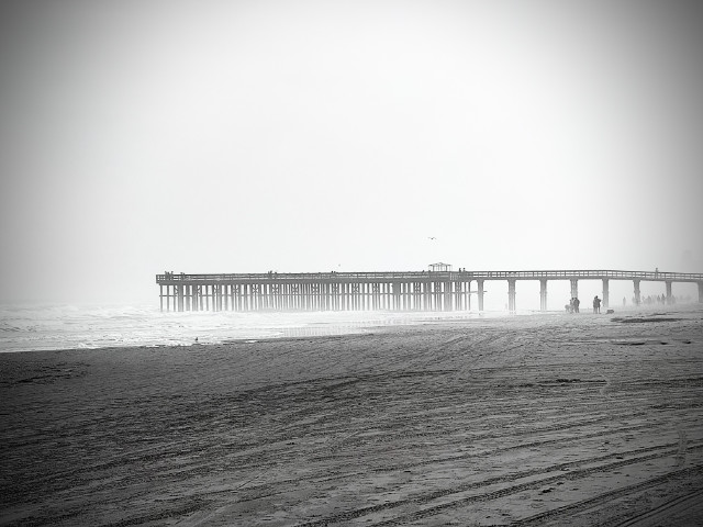 Photo: black-and-white scene of a pier extending into the Gulf of America at South Padre Island, TX